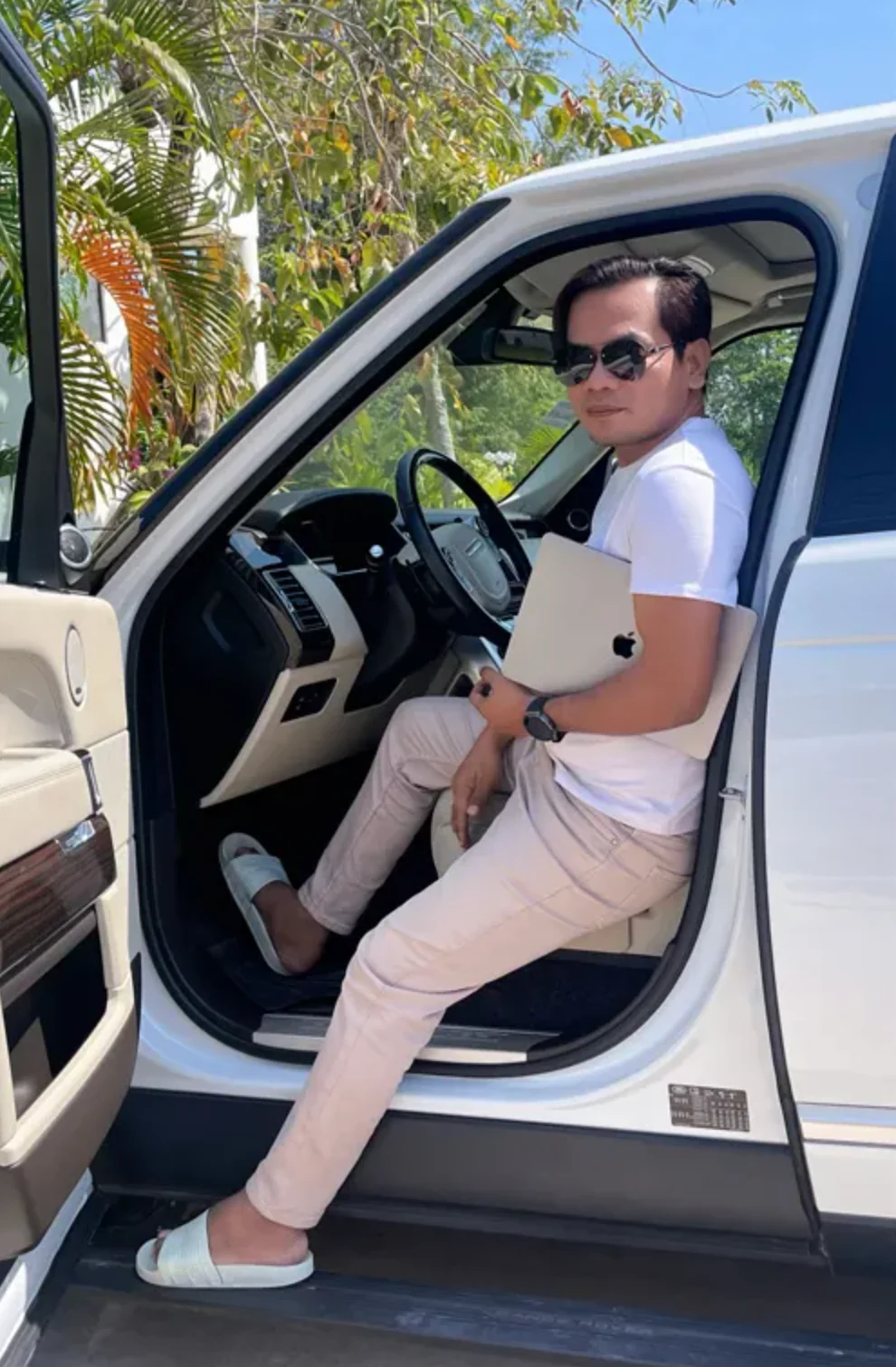 Cambodia POS System — Mr. Andy Sim, founder of BrownPOS, in a white T-shirt with his laptop, sitting in the open door of a car under palm trees